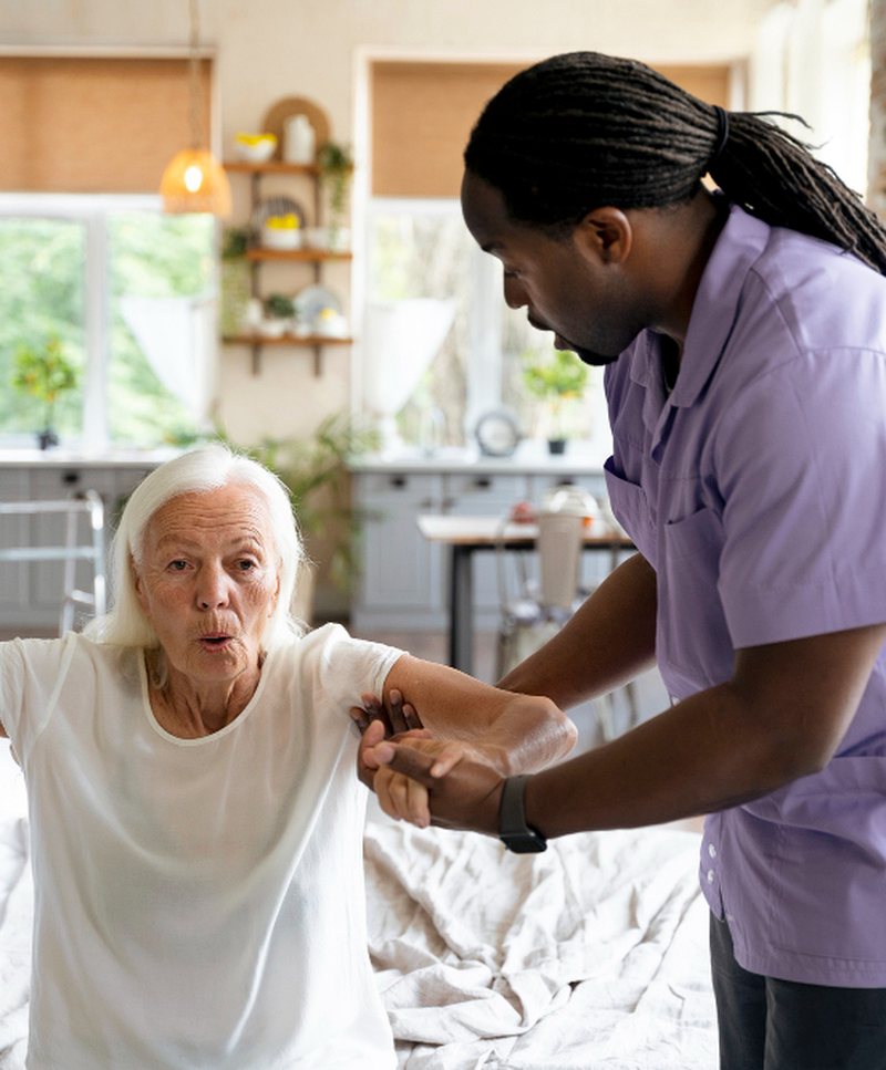 A caregiver supporting a client as she gets up, with her walking cane to hand